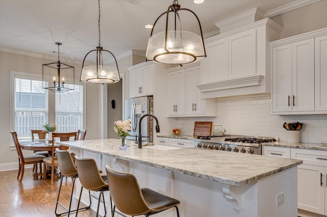 kitchen featuring hanging light fixtures, freestanding refrigerator, an island with sink, and white cabinetry