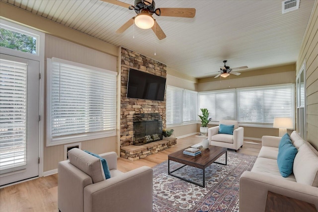 living room featuring light wood finished floors, visible vents, a ceiling fan, a stone fireplace, and baseboards