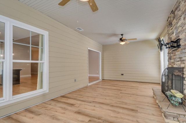 interior space featuring visible vents, a stone fireplace, wood finished floors, and a ceiling fan