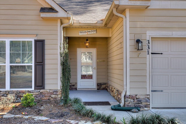 view of exterior entry with a garage, stone siding, and roof with shingles