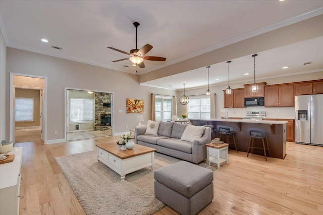 living area with ceiling fan, light wood-style flooring, visible vents, baseboards, and ornamental molding