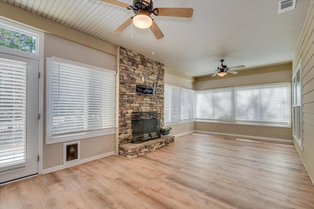 unfurnished living room with visible vents, ceiling fan, a stone fireplace, and wood finished floors