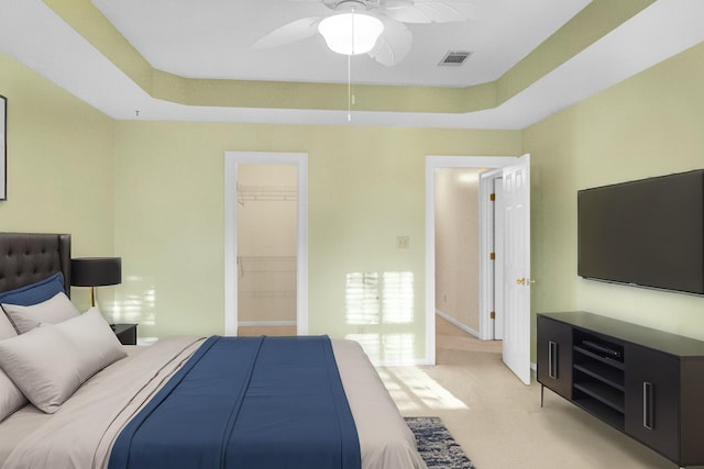 bedroom featuring a tray ceiling, light colored carpet, ceiling fan, a spacious closet, and a closet