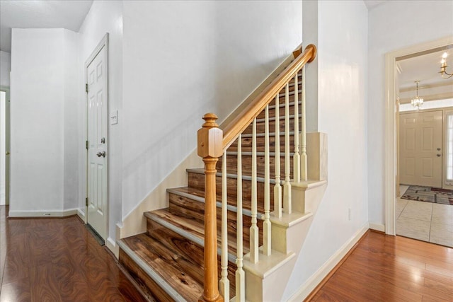 stairs featuring baseboards, wood finished floors, and a chandelier