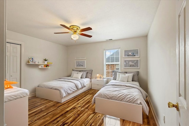 bedroom with wood finished floors, baseboards, ceiling fan, and a closet