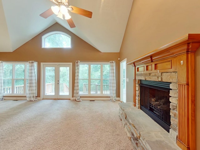 unfurnished living room with french doors, a stone fireplace, ceiling fan, and light carpet