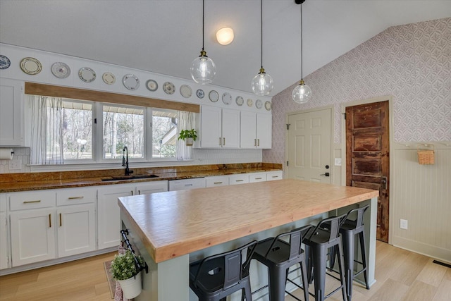 kitchen with butcher block counters, wallpapered walls, lofted ceiling, and a sink