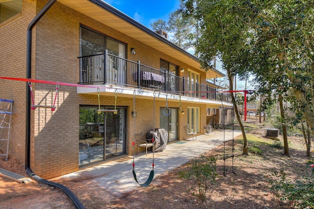 rear view of house with a patio, a balcony, brick siding, and central air condition unit