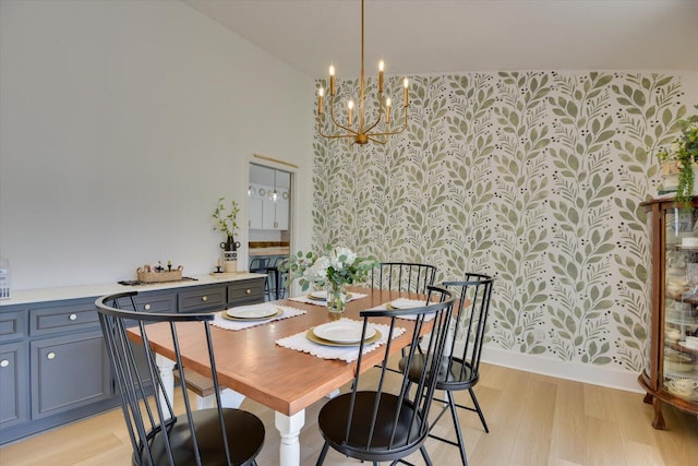 dining area with wallpapered walls, an inviting chandelier, light wood-style flooring, and a towering ceiling