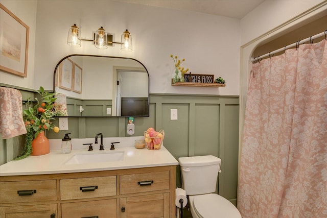 full bathroom featuring a wainscoted wall, toilet, a shower with shower curtain, a decorative wall, and vanity