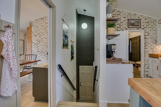 hallway with an upstairs landing, light wood-style floors, lofted ceiling, and ornamental molding