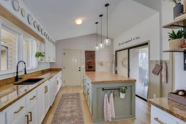 kitchen with wallpapered walls, vaulted ceiling, white cabinets, and a sink