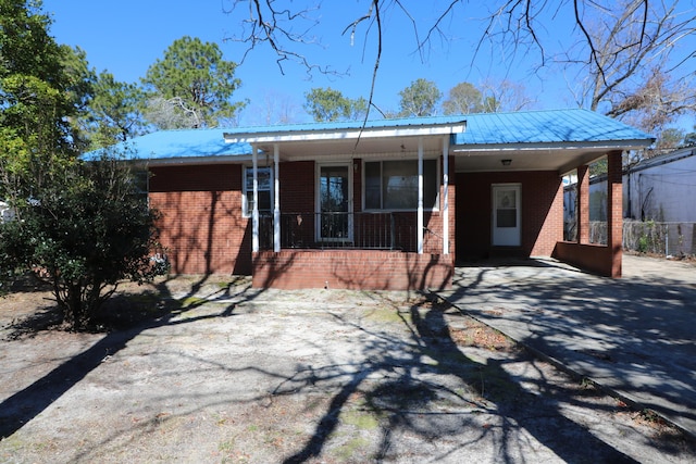 ranch-style home with metal roof, an attached carport, covered porch, brick siding, and concrete driveway