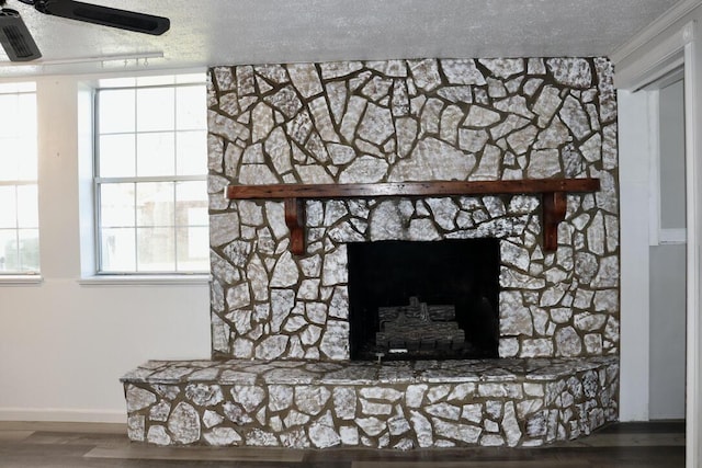 room details featuring a ceiling fan, a textured ceiling, wood finished floors, a stone fireplace, and baseboards