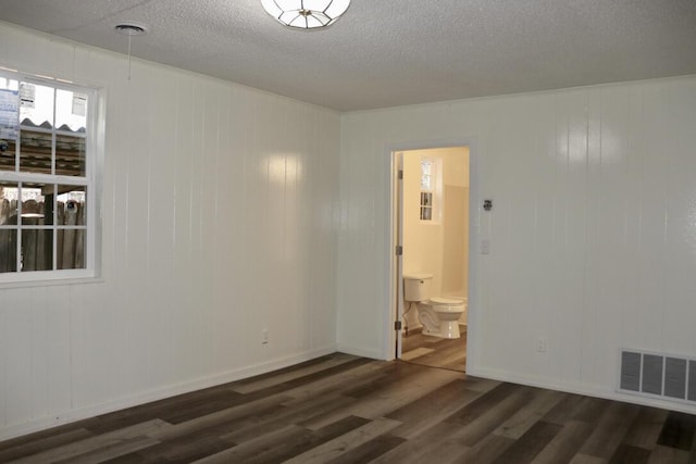 unfurnished room with dark wood finished floors, baseboards, visible vents, and a textured ceiling