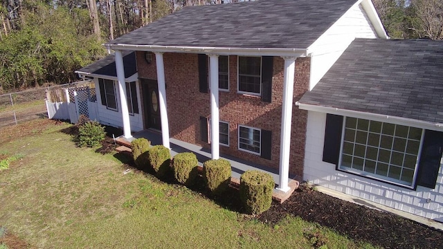 view of home's exterior featuring a lawn, a shingled roof, and fence