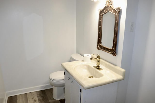 half bath with vanity, toilet, wood finished floors, and baseboards