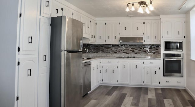 kitchen with under cabinet range hood, appliances with stainless steel finishes, an inviting chandelier, wood finished floors, and white cabinets