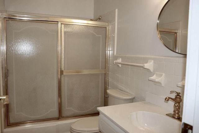 full bath featuring vanity, a wainscoted wall, shower / bath combination with glass door, tile walls, and toilet