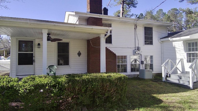 back of house featuring central AC unit, a ceiling fan, a lawn, and a chimney