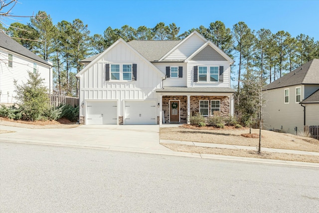 view of front of property featuring driveway, stone siding, an attached garage, covered porch, and board and batten siding