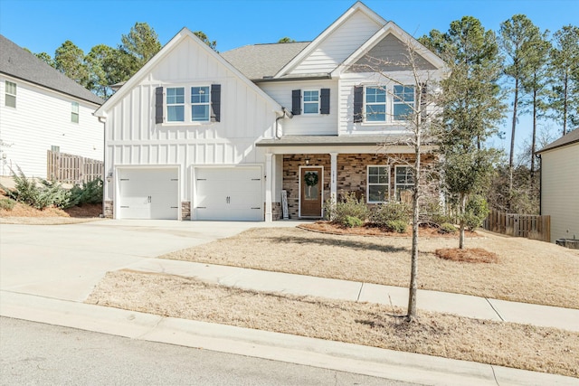 view of front of home with driveway, stone siding, an attached garage, fence, and board and batten siding