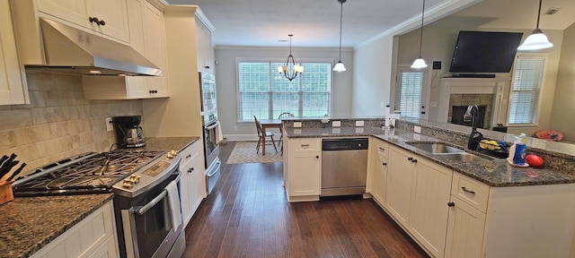 kitchen with stainless steel appliances, a stone fireplace, dark stone countertops, and decorative light fixtures