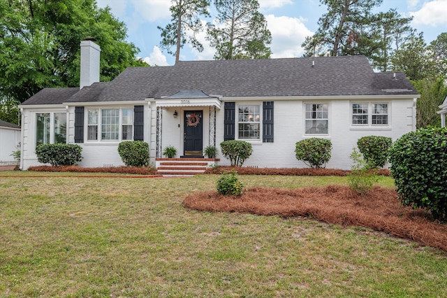 single story home with brick siding, a shingled roof, a front lawn, and a chimney