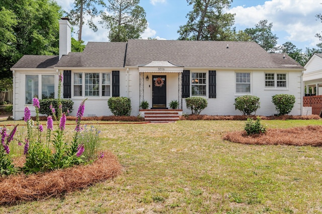 single story home featuring brick siding, a chimney, a shingled roof, and a front yard