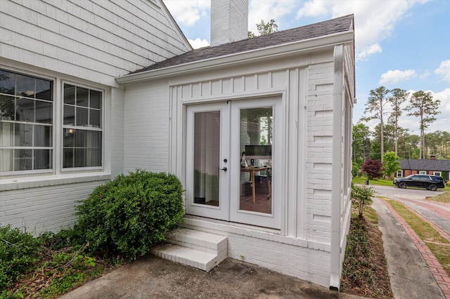 entrance to property featuring french doors, a chimney, and brick siding