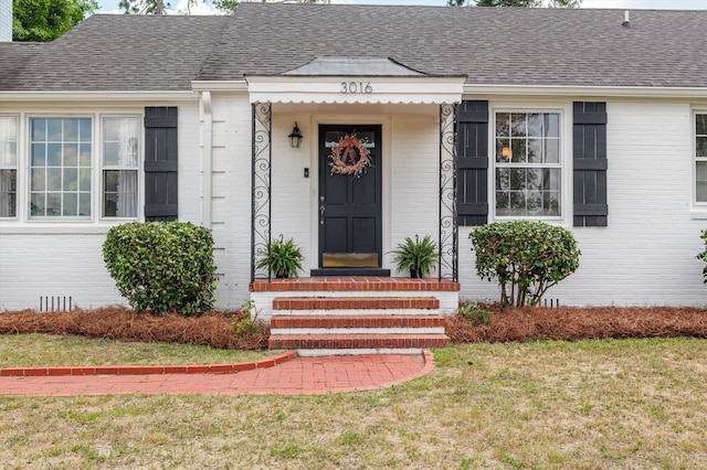 property entrance with a lawn, brick siding, and roof with shingles