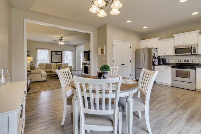 dining space with ceiling fan with notable chandelier and light wood-type flooring