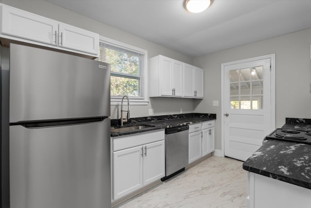 kitchen with white cabinets, stainless steel appliances, dark stone counters, and sink