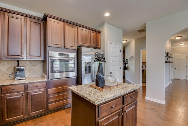 336 Shell Brooke Way, Lexington, SC 29073 - kitchen featuring appliances with stainless steel finishes, arched walkways, light wood-style flooring, light stone countertops, and tasteful backsplash