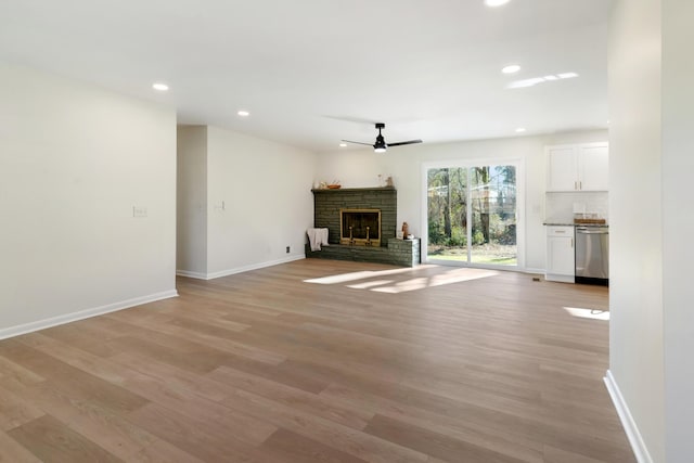 unfurnished living room featuring a stone fireplace, ceiling fan, and light wood-type flooring