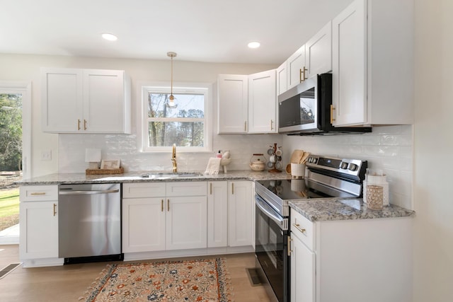 kitchen featuring light stone counters, stainless steel appliances, sink, decorative light fixtures, and white cabinets