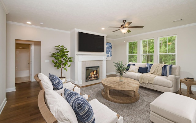 living room featuring crown molding, a tiled fireplace, visible vents, and wood finished floors