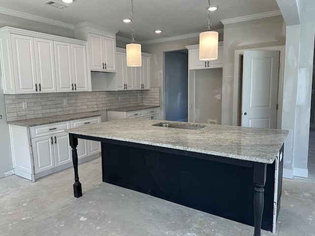 kitchen with white cabinets, unfinished concrete flooring, a kitchen island with sink, crown molding, and backsplash