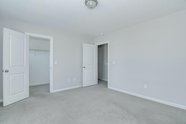 unfurnished bedroom with a closet, carpet flooring, a spacious closet, and baseboards