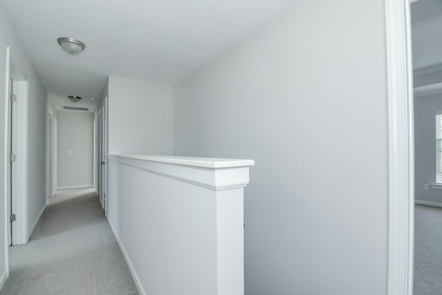 hallway featuring an upstairs landing, light colored carpet, and baseboards