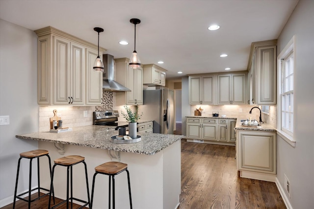 kitchen featuring cream cabinets, wall chimney exhaust hood, decorative light fixtures, and appliances with stainless steel finishes