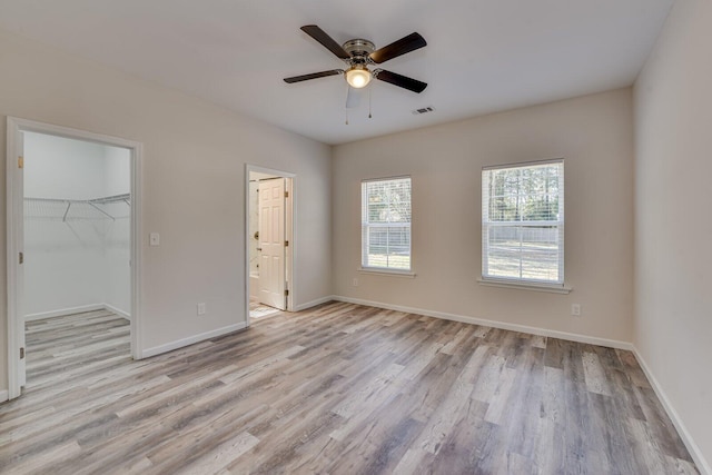 unfurnished bedroom featuring baseboards, visible vents, ensuite bath, a spacious closet, and light wood-style floors