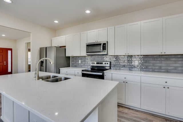 kitchen featuring stainless steel appliances, a sink, white cabinetry, backsplash, and an island with sink