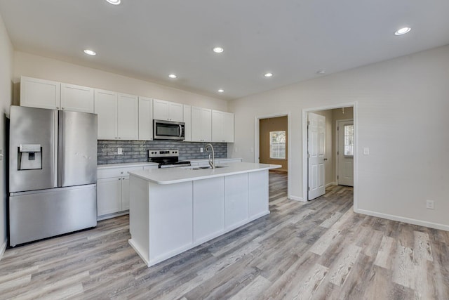 kitchen featuring tasteful backsplash, appliances with stainless steel finishes, light countertops, light wood-style floors, and a sink