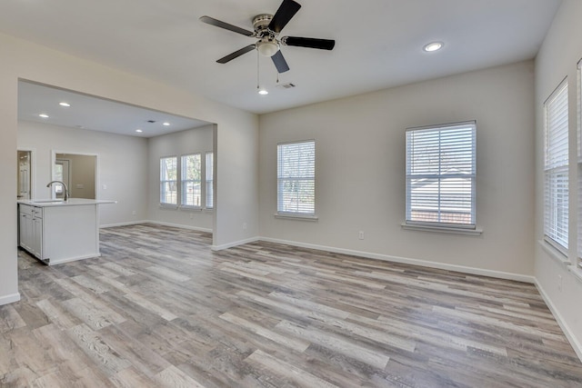 unfurnished living room featuring light wood-style floors, visible vents, a sink, and baseboards