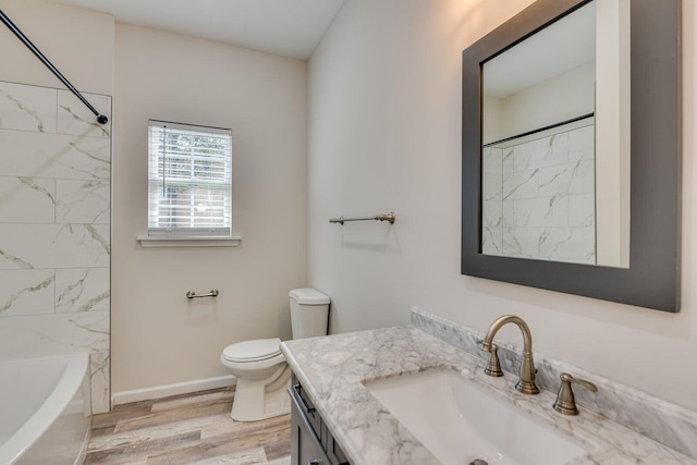 bathroom with baseboards, bathing tub / shower combination, toilet, wood finished floors, and vanity