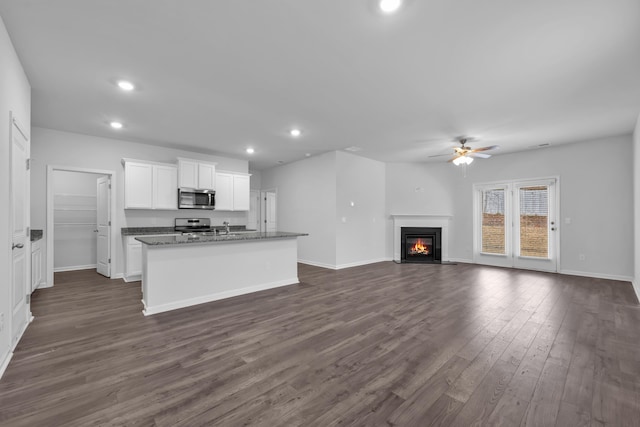 kitchen with dark wood-type flooring, white cabinets, a center island with sink, ceiling fan, and stainless steel appliances