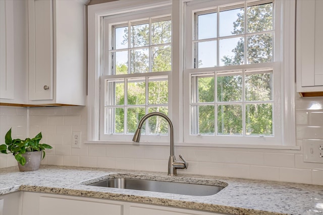 room details featuring white cabinets, light stone countertops, decorative backsplash, and a sink