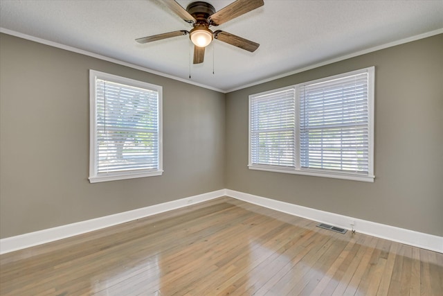 spare room with baseboards, visible vents, a ceiling fan, crown molding, and wood-type flooring