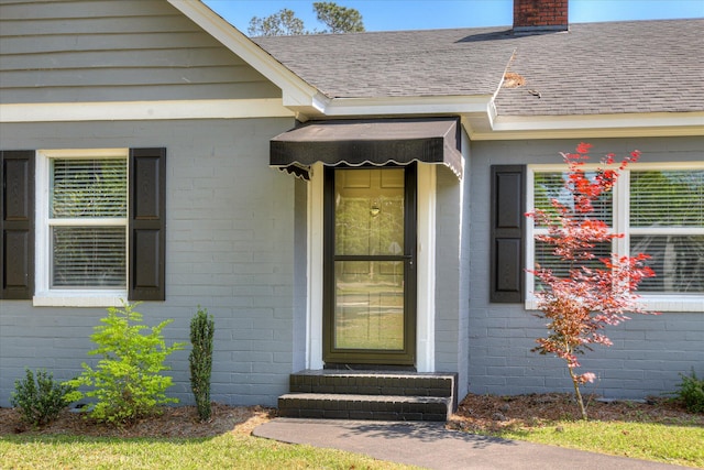 entrance to property with brick siding, a shingled roof, and a chimney